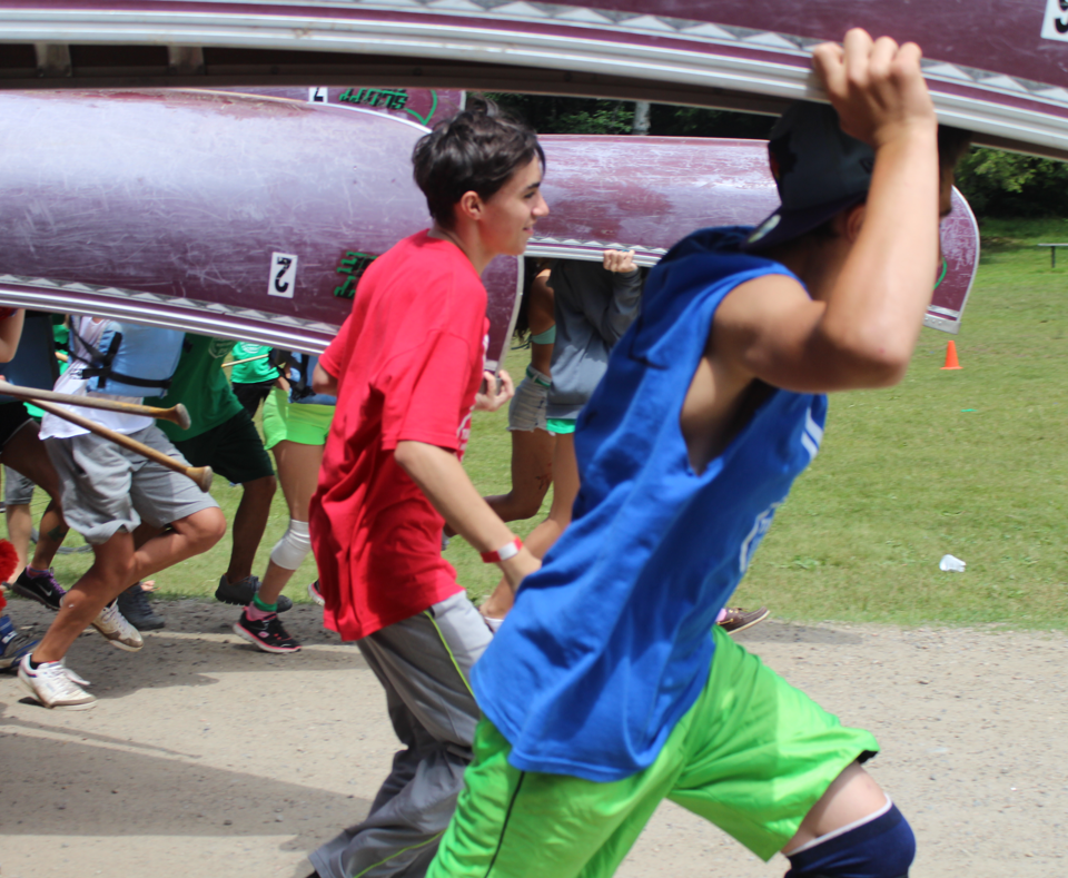 Group of boys holding a canoe over their head and walking